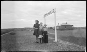 Four children stand on the abandoned rail platform at Lennonville, Railway building in the background. 1950