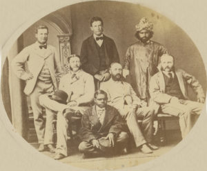 Ernest Giles Exploring Expedition, 1875, from left to right: Standing: Peter Nicholls, Alec Ross and Saleh. Sitting on chairs: Jess Young, Ernest Giles, and W.H Tietkens. Sitting on floor: Tommy Oldham [