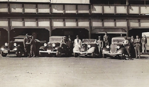 Mick and Barney (leaning on car at extreme right) enjoy a drink with mates outside the Commercial Hotel, Wiluna. (Note the beer bottles on the bonnets of two cars and the water bags on the front bumpers of two other vehicles.)