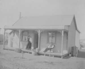 House in Trafalgar, Man seated in chair Douglas William GRAY and woman standing holding small child May Elizabeth nee Gilholm. House is small cottage with iron roof