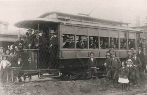 Single truck car 4 and its load of male passengers is surrounded by onlookers as it is photographed during the official opening of the Kalgoorlie tramways on 20 May 1902. Mr Stanley hold the lever.