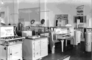 A pre-decimal currency display of gas, slow combustion and wood stoves in the showroom of J.Fitzpatrick & Co, the Thermett gas stove on the left available for nine pounds deposit and fourteen shillings weekly.