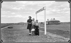 Four children stand on the abandoned rail platform at Lennonville, with the railway building in the background. 1950 - Photo SLWA